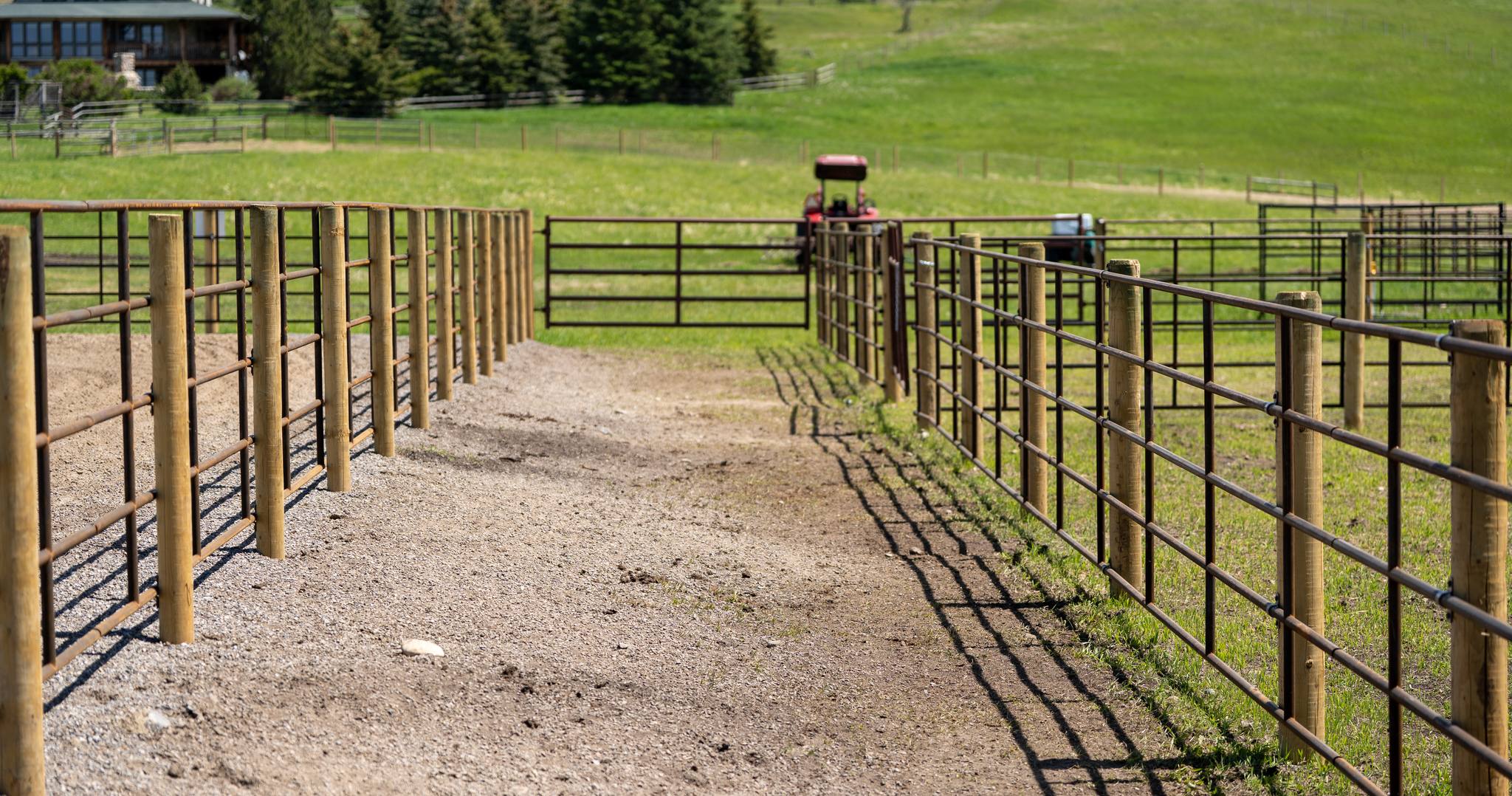 Laneway between Ranchcore panel fence runs with a tractor working beyond the gate